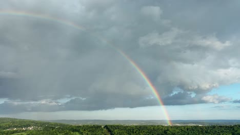 A-left-panning-aerial-view-of-a-rainbow-after-a-thunderstorm-over-the-beautiful-green-countryside