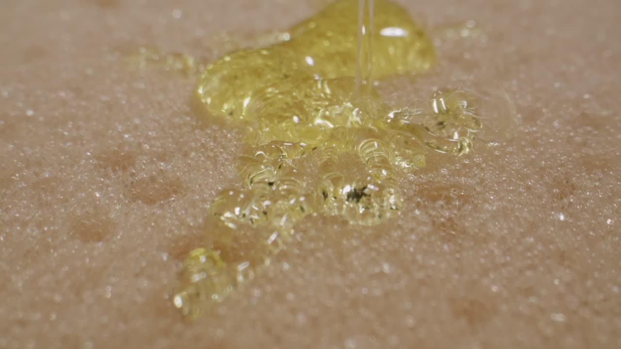 Close Up of Golden Oil Pouring and Absorbing into Foam