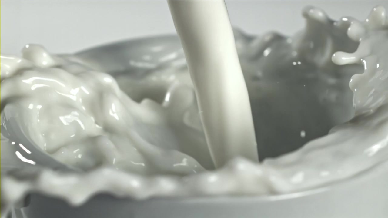 白いカップに牛乳が注がれ、水しぶきを上げるスローモーションのクローズアップ。