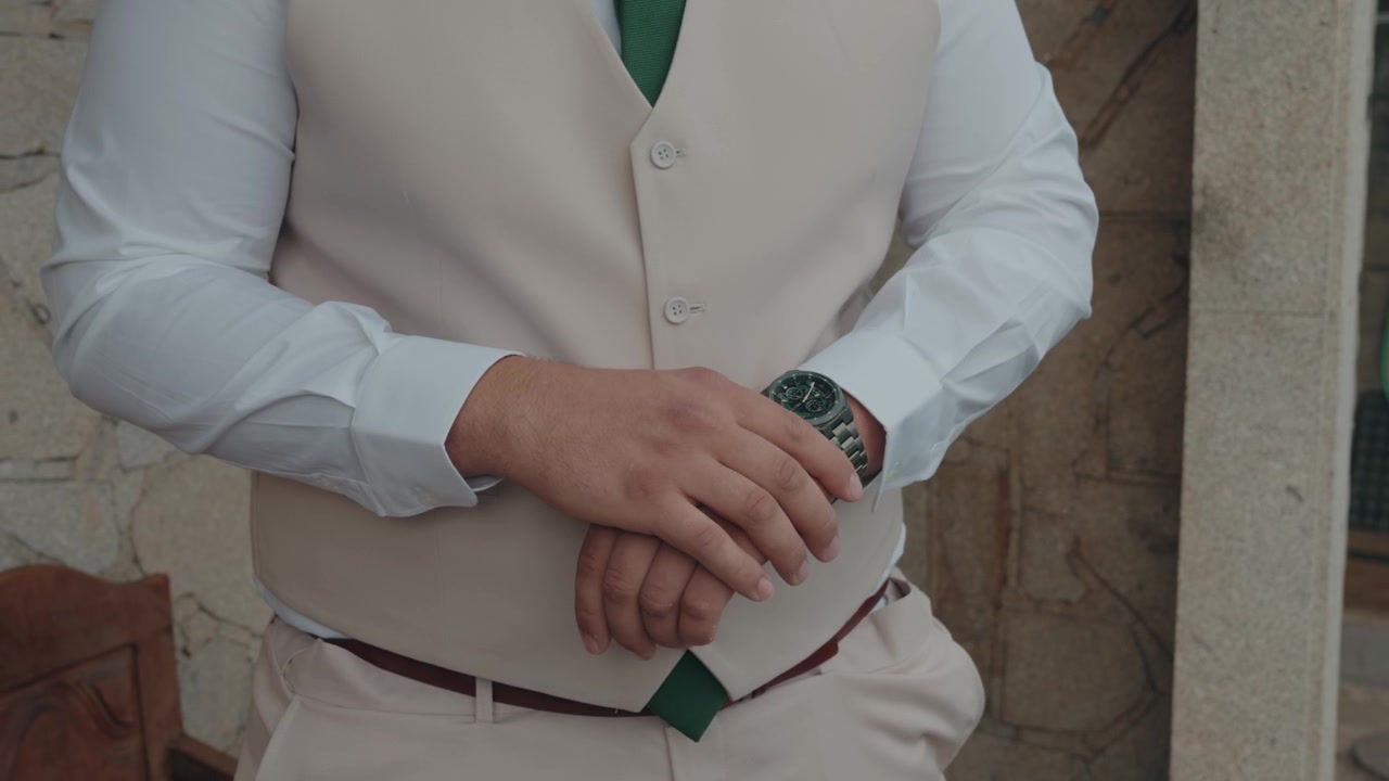 Yelek ve gömlek giymiş damat ellerinin kol saatini ayarlarken yakın çekimi.