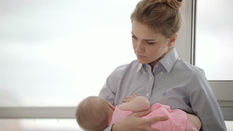 madre cansada sosteniendo al bebé en las manos cerca de la ventana. mujer cansada sosteniendo al niño