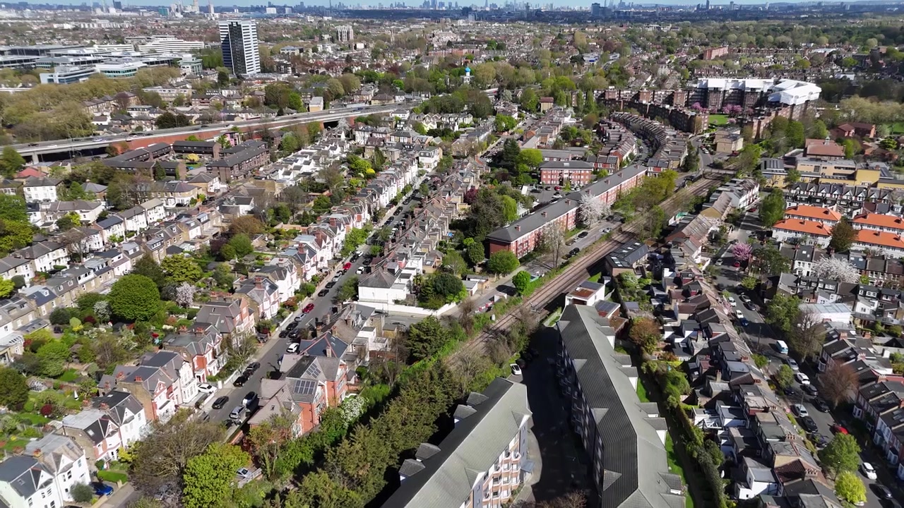 Dichte straten met rijtjeshuizen en volwassen bomen verspreid over een groene buitenwijk, met de stadsskyline ver weg aan de horizon.