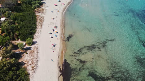 Bird's-Eye-View-Of-Mediterranean-Sea-With-Tourists-Under-Colorful-Umbrellas-At-Sunny-Sandy-Beach-Of-Sardinia,-Italy