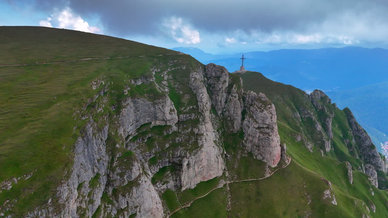 Stunning mountain with cross. A stunning view of a rocky mountain ridge topped with a cross, surrounded by lush green hills and a dramatic sky