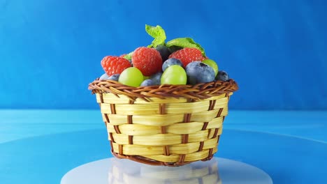 rotating wooden basket with different forest berries close-up on a blue wooden table. 4k slow motion loop video.