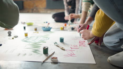 close up of unrecognizable environmental activists painting placards sitting on the floor