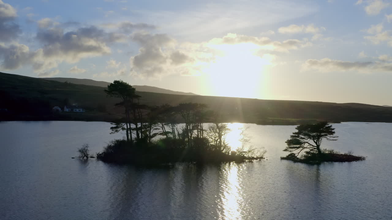 Aerial of backlit small island in Lough Bofin at dawn, the lake’s peaceful waters and soft morning glow, Connemara, Galway, Ireland