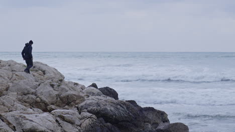 man strides confidently over rocks towards crashing waves and he captures a photograph as they surge and foam against the shore