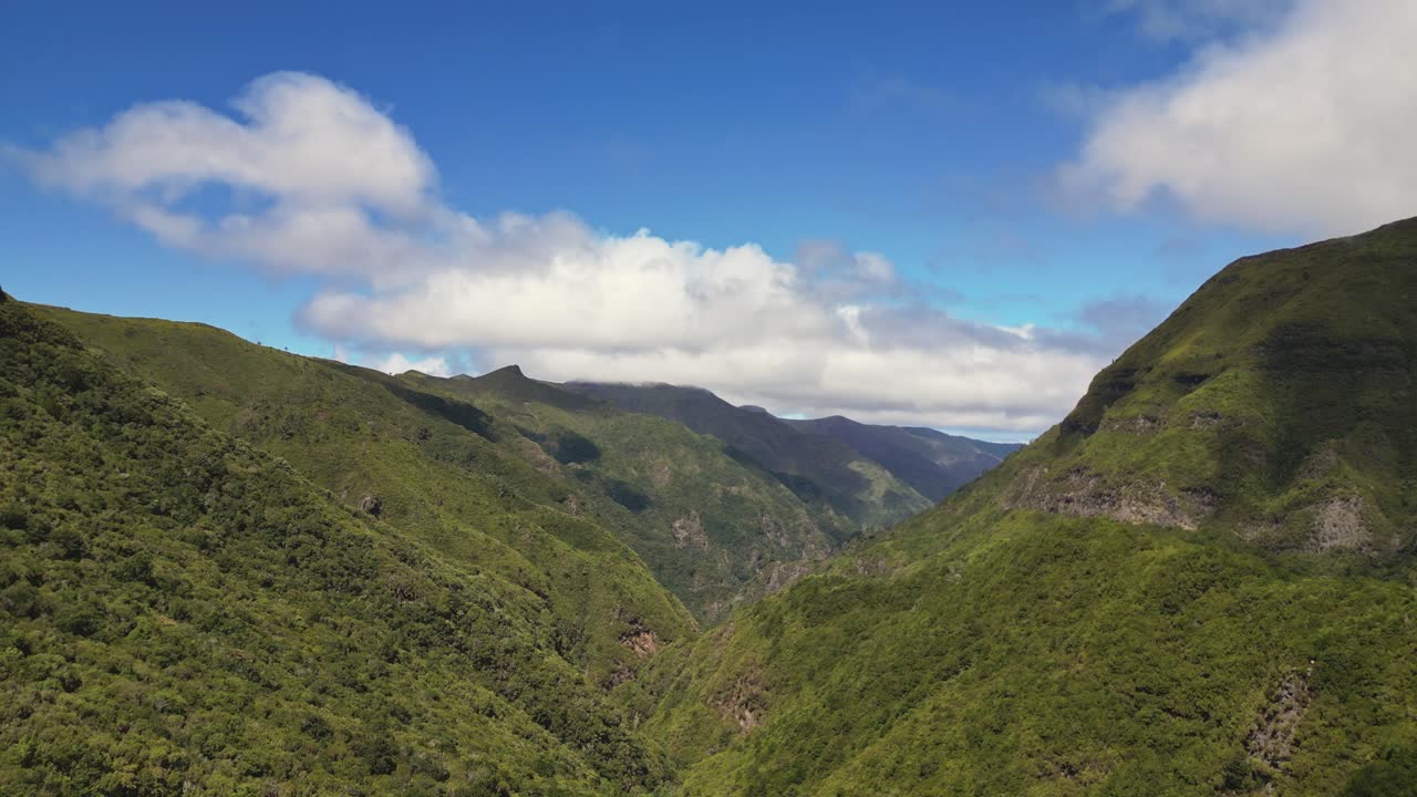 Aerial view of lush green mountains in Madeira, Portugal under blue sky with clouds and deep valleys