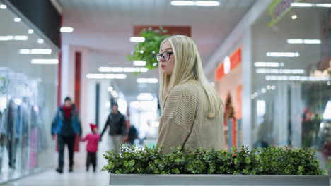 career woman sipping tea while looking thoughtfully with decorative flower nearby. in the background, a family walks together in a mall, creating a vibrant and bustling atmosphere