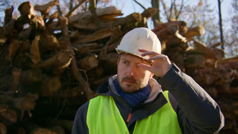 Male-logger-standing-in-front-of-large-group-of-cut-tree-trunks