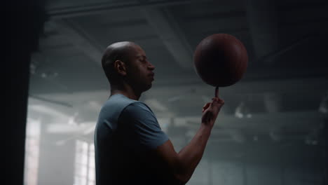 retrato de un jugador de baloncesto serio girando una pelota de baloncesto en el dedo en el gimnasio