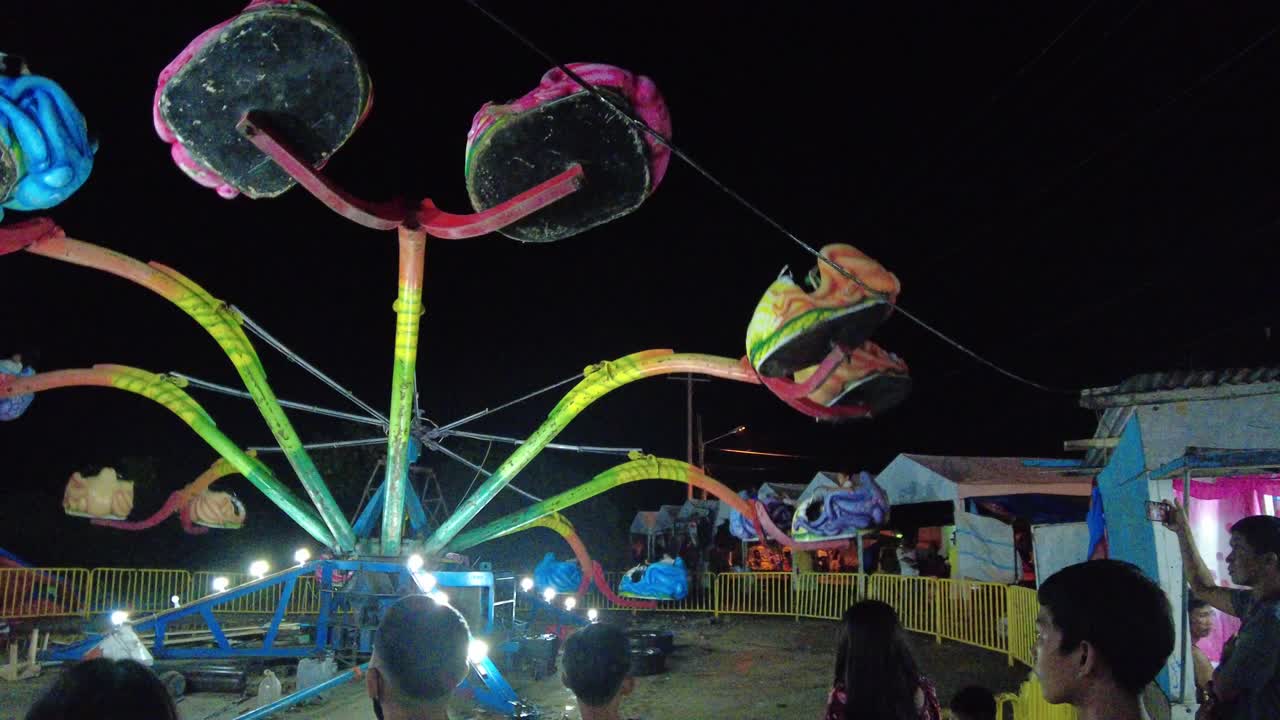 A dynamic shot of an octopus ride in an amusement park while repeatedly moving the passengers up and down to add thrill and excitement to their experience.