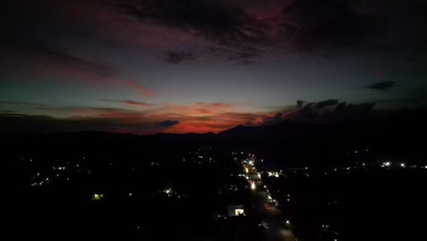 Aerial-panoramic-view-of-red-sunset-over-urban-street-with-car-headlights-driving