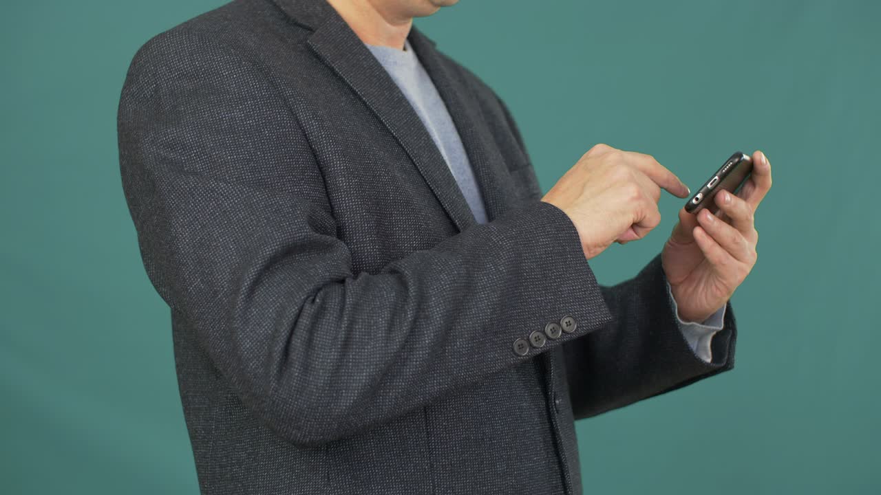 비즈니스맨이 녹색 배경에서 인터넷을 서핑하기 위해 스마트폰 화면을 만지고 있습니다.