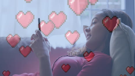 animación de iconos digitales de corazón sobre una mujer que usa un teléfono inteligente en casa