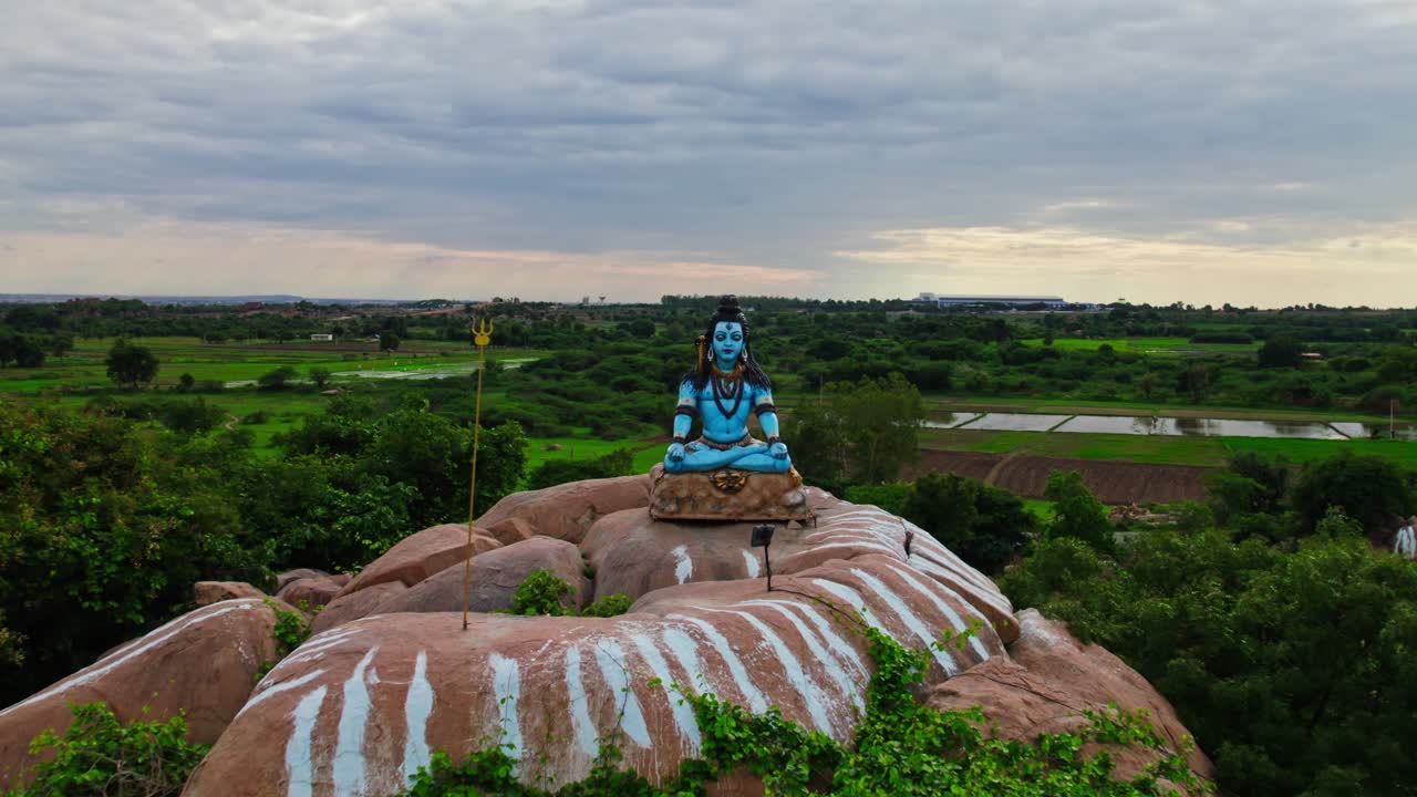 lord shiva statue on the top of granite stone in the background crop fields lands, push back, drone shot, 4k.