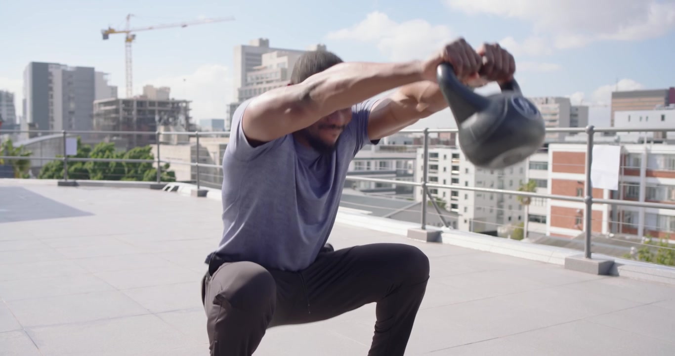 Uomo afroamericano che sposta il peso, facendo oscillare un kettlebell sul tetto per aumentare la forza.