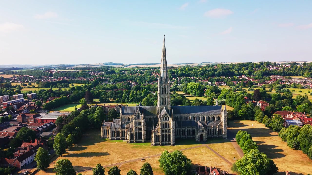 Szeroki widok z drona na Katedrę w Salisbury i jej średniowieczną iglicę, otoczoną historycznymi budynkami, zielonymi terenami i wiejskim krajobrazem Wiltshire w pogodny letni dzień