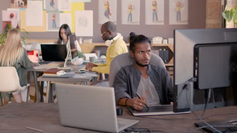 diseñador gráfico masculino que usa una tableta de dibujo digital y mira el monitor de la computadora en un estudio de animación