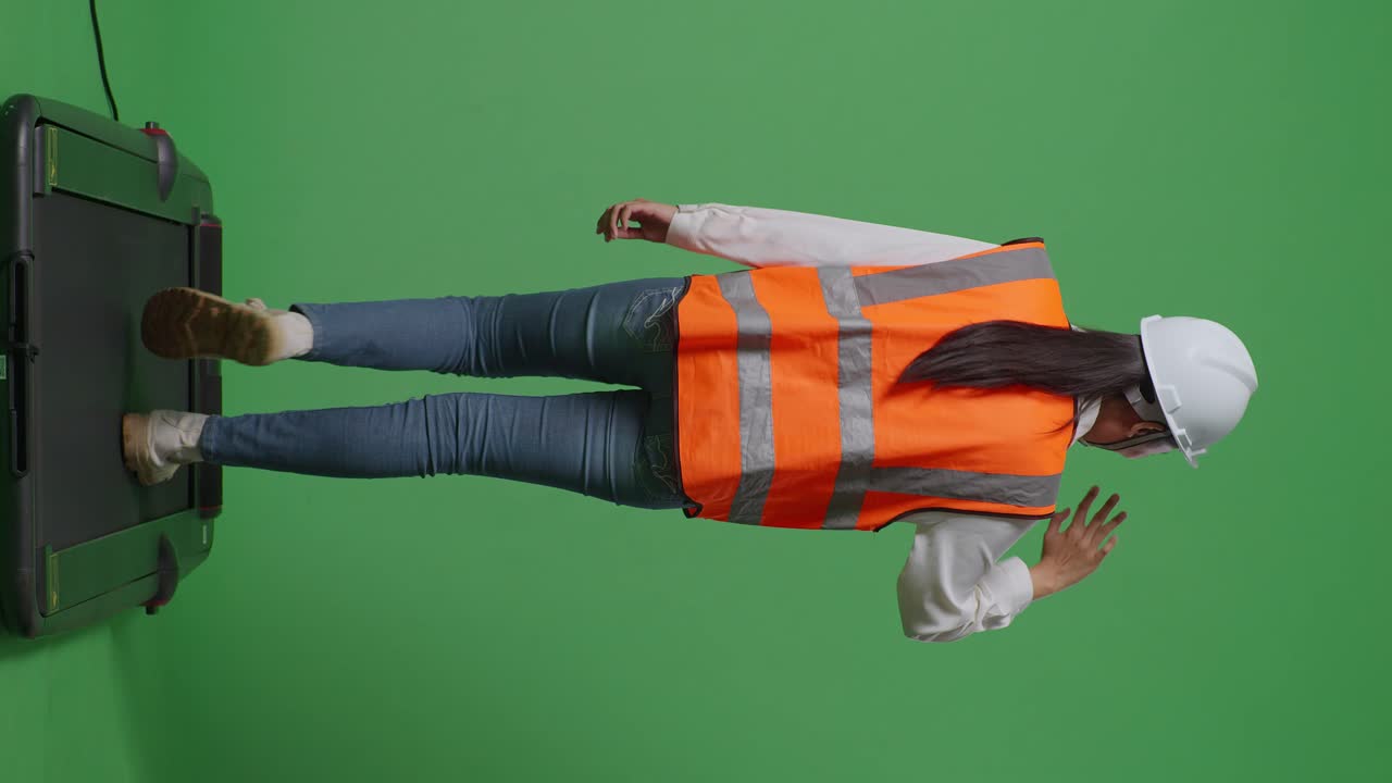 안전 헬을 입은 아시아 여성 엔지니어가 녹색 화면 배경 스튜디오에서 는 동안 손을 흔들고 있는 모습