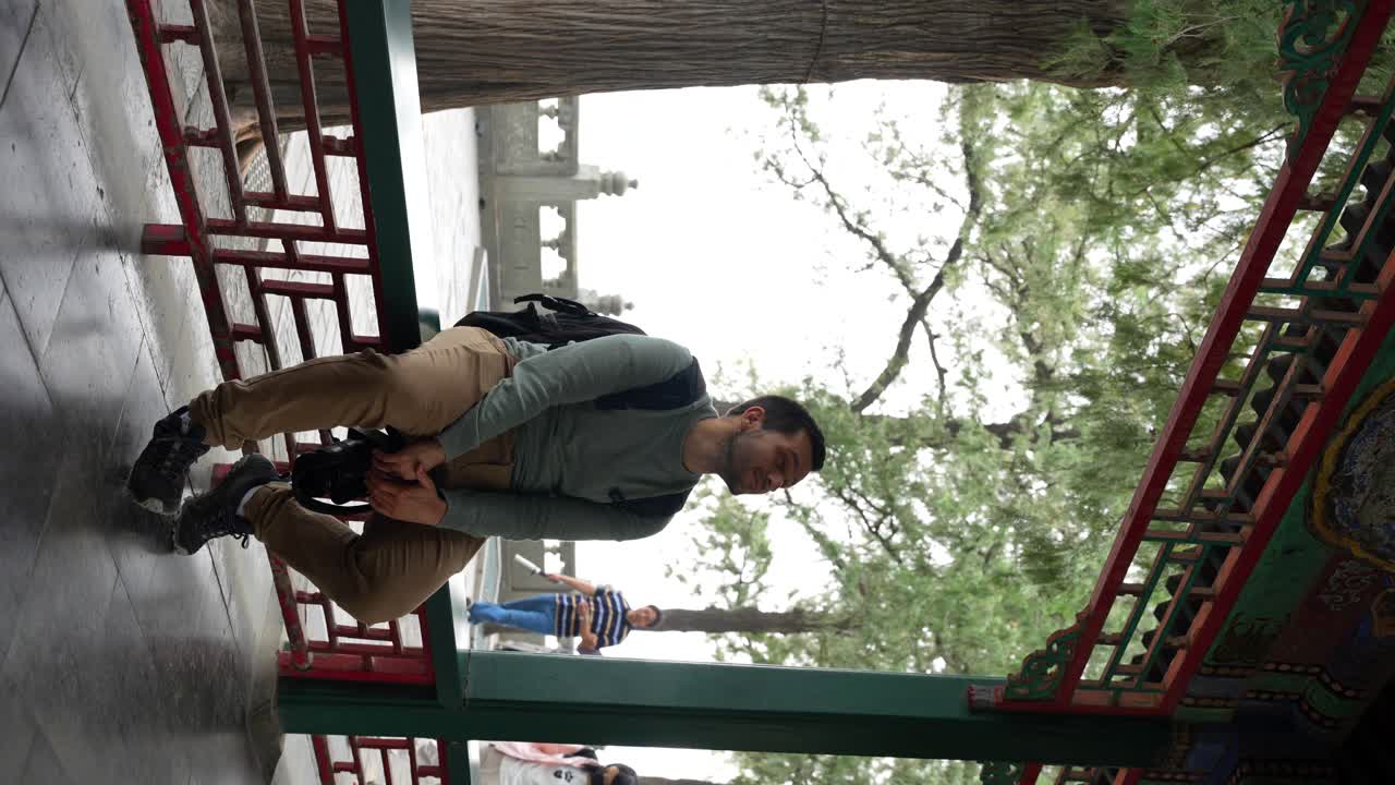Man sits on a bench in the Long Corridor of the Summer Palace, as people walk behind, Beijing. Vertical