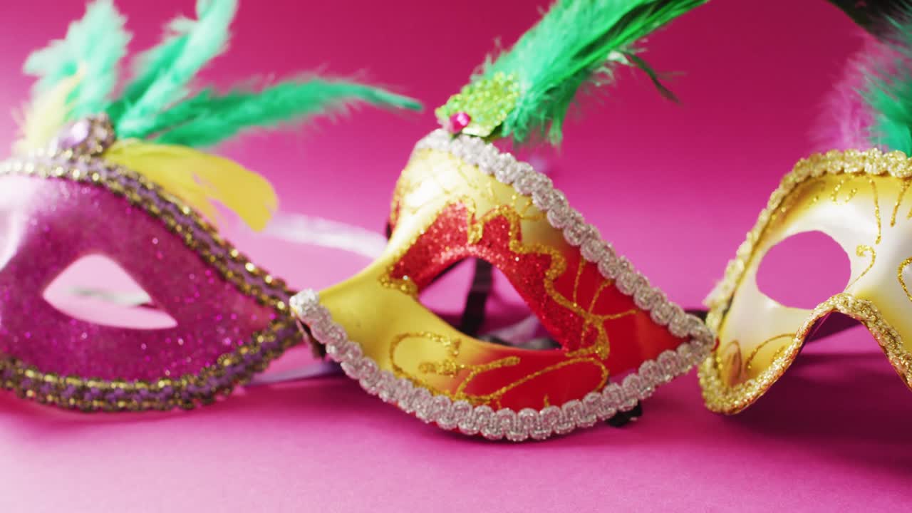 Video of three carnival masquerade masks with green feathers on pink background