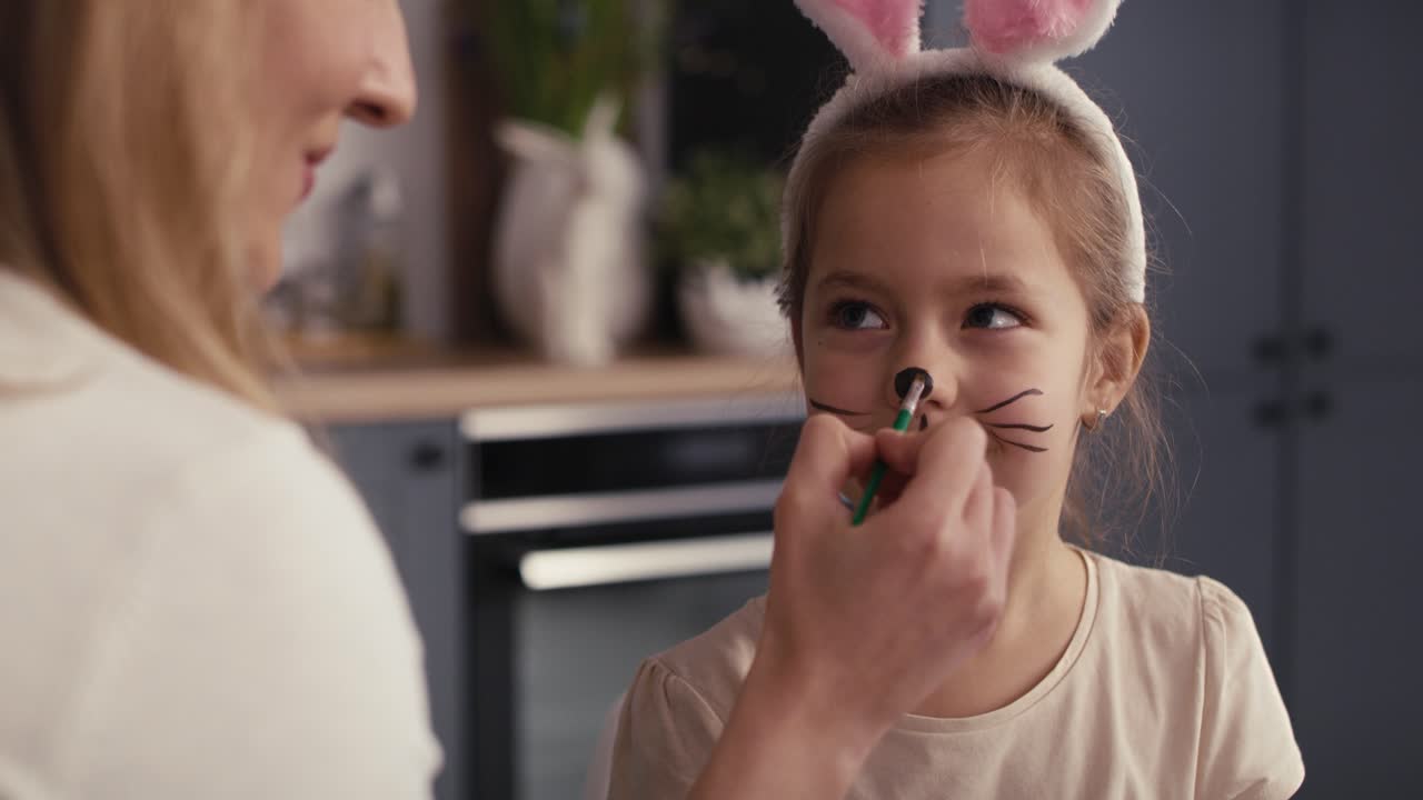 Caucasian mother and daughter painting Easter bunny on girl's face.