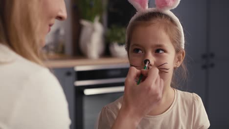 caucasian mother and daughter painting easter bunny on girl's face.