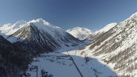 Toma-Aérea-De-Un-Valle-De-Montaña-Bajo-El-Sol-Y-La-Nieve