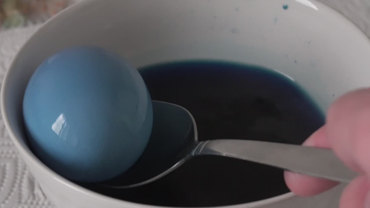 Painting an eastern egg in a bowl of water and blue color