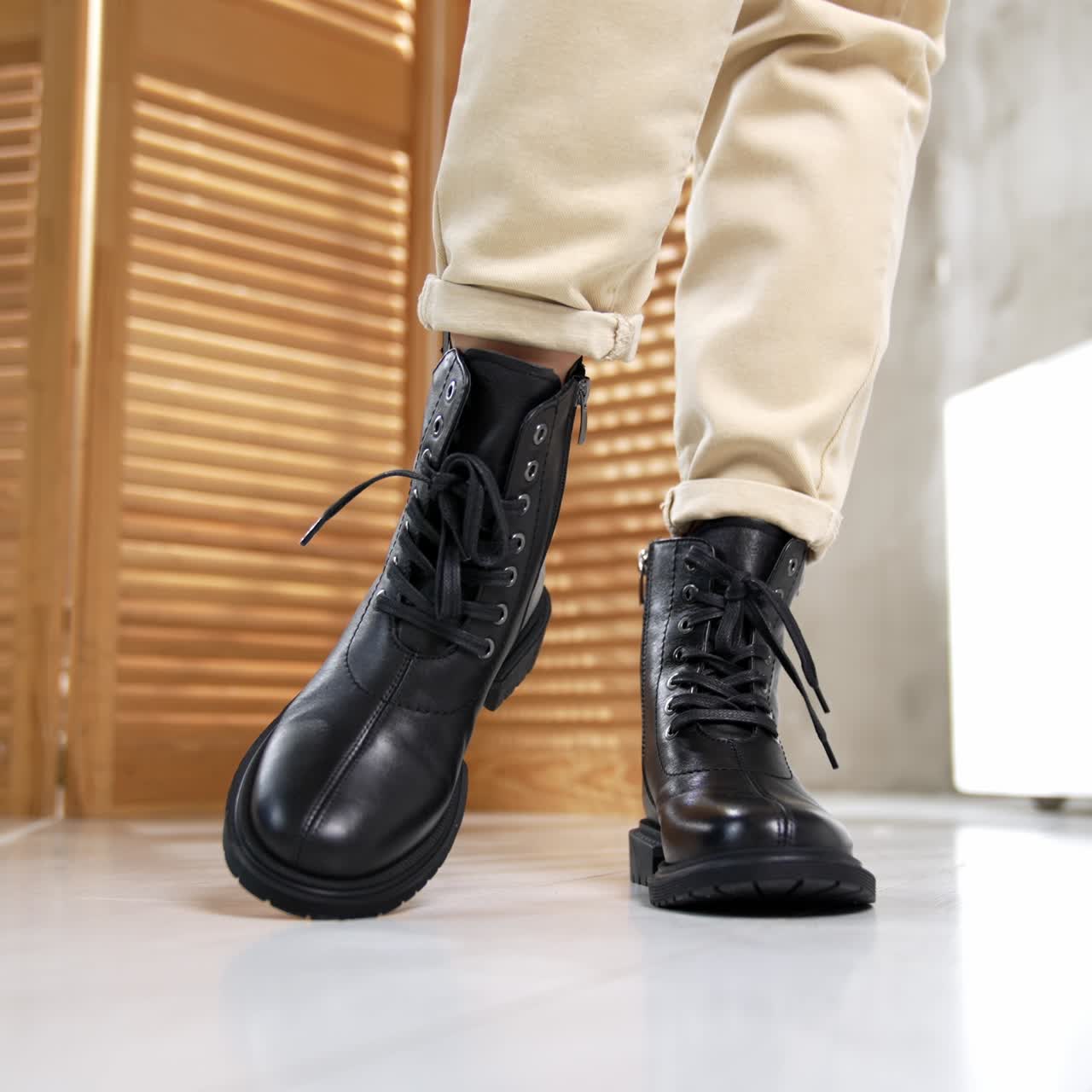Woman in light jeans presents the black footwear with laces. Modern boots on a plain sole and rounded nosepieces close up. Studio backdrop