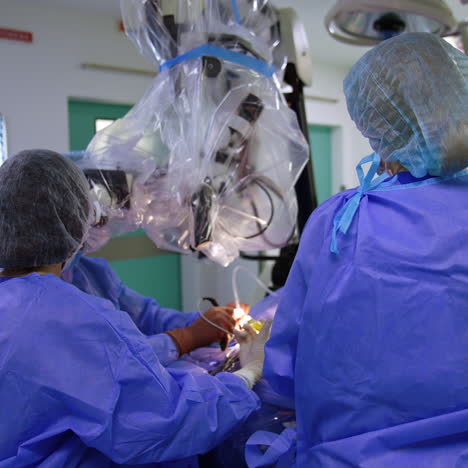 rear view of the medics working in modern surgery room. doctors perform neurosurgical procedure using powerful microscope.