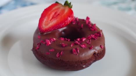 delicious chocholate donut with strawberry and sprinkles slowly rotating on white plate