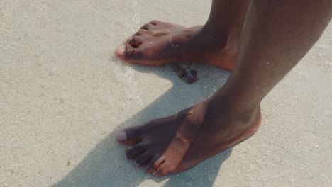 the bare ankles and feet of a black person stepping into the white sands of an ocean beach