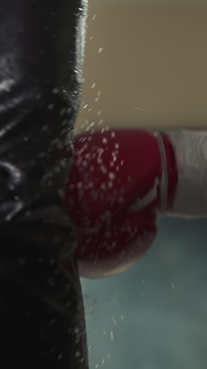 Man boxing expert using hand in glove strikes punching bag with droplets of water. Engaging in combat sports and enhancing strength in dark gym