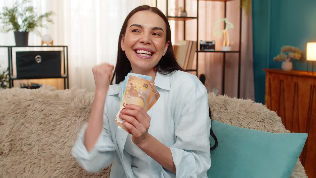 Giovane donna sul divano che conta euro in contanti, sorridendo felicemente e soddisfatta mentre riceve stipendio o reddito