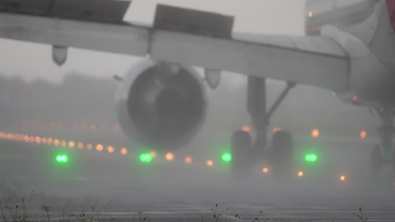 Primer plano del tren de aterrizaje y el motor de una aeronave en la pista durante una lluvia intensa.