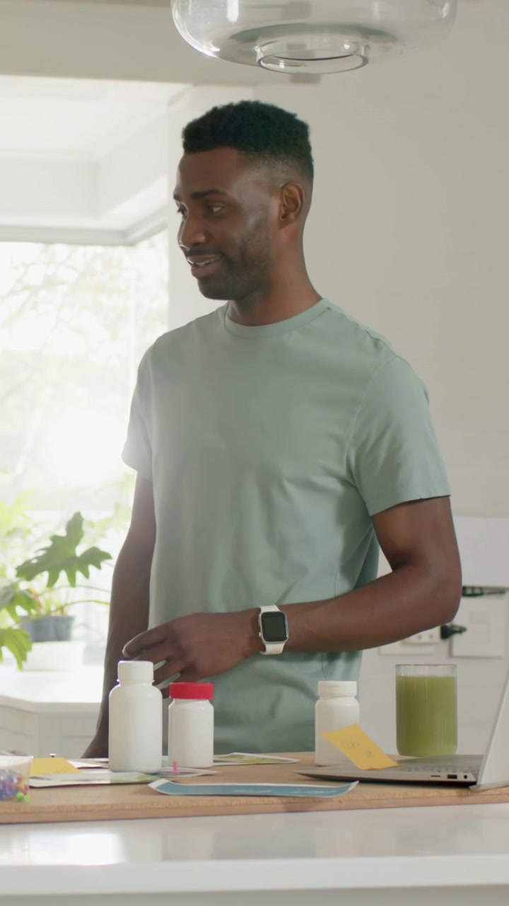 Vertical video: Hearing offscreen voice, man in green tee touching bottles in kitchen, smiling