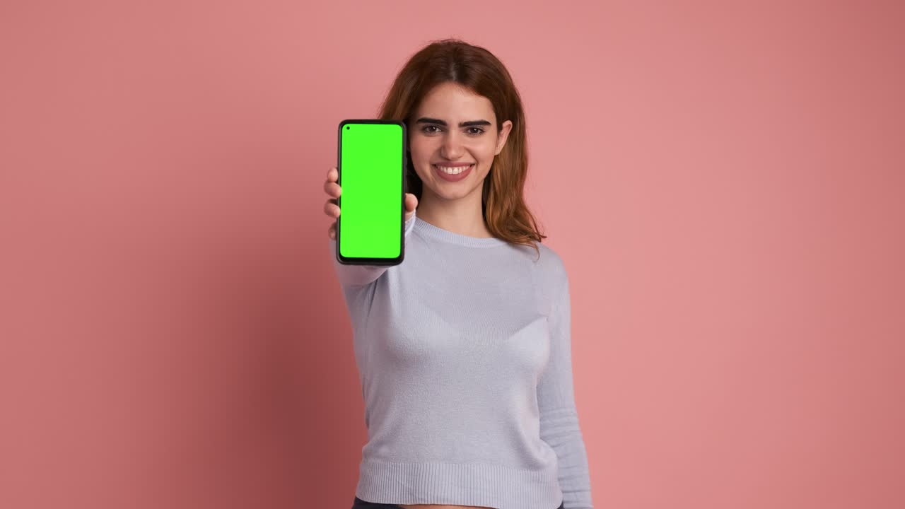 Woman showing cellphone with green screen in studio