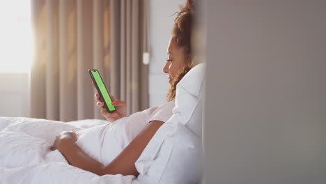 woman sitting up in bed looking at mobile phone after having woken up