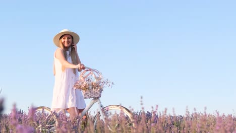 Beautiful French Woman in a White Dress and a White Hat on a Lavender Field Beautiful French Woman in a White Dress and a White Hat on a Lavender Field a Blonde with a Bicycle Fixes her Hair against the Background of the Blue Sky