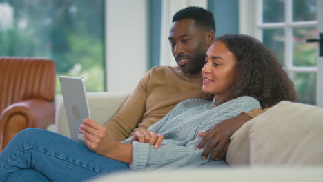 young couple relaxing on sofa at home using digital tablet together