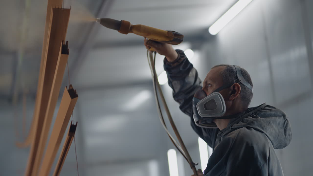 Molar's portrait sprays paint on steel profiles in a respirator mask and protective suit in slow motion. Production and painting studio