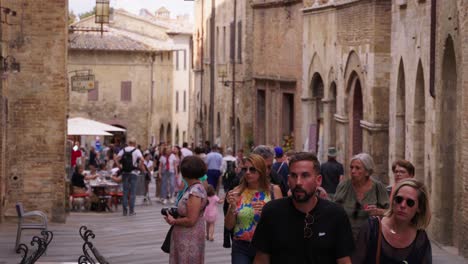 stabilized shot of people walking on a street surrounded by old buildings in tuscany, italy, on a cloudy day.