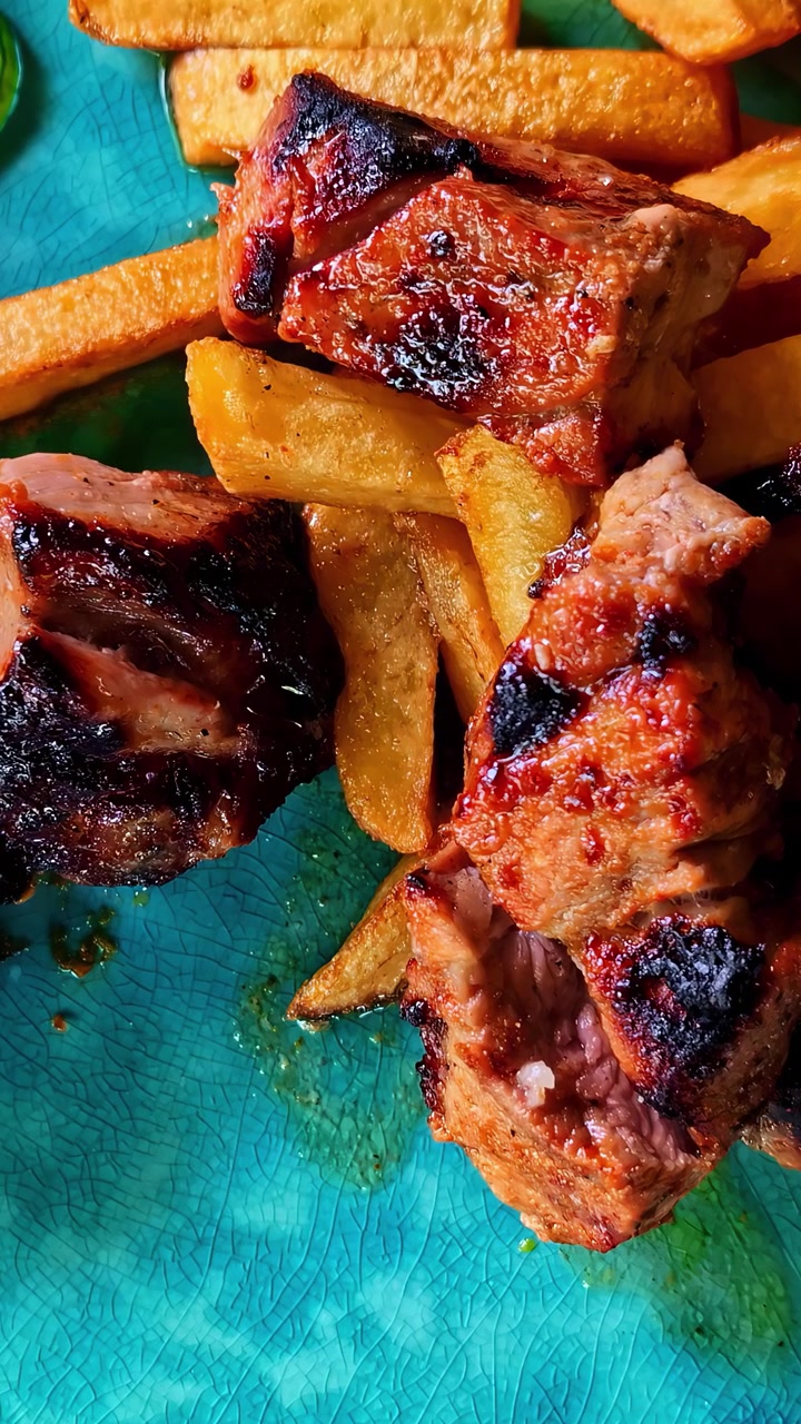 Scatto macro di autentici spiedini di maiale alla griglia e patatine fritte dorate serviti su un vivace piatto di ceramica turchese. Presentazione cinematografica del cibo per contenuti di ristorazione e culinari