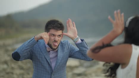 una pareja de bodas de pie cerca del río de la montaña. el novio y la novia haciendo caras