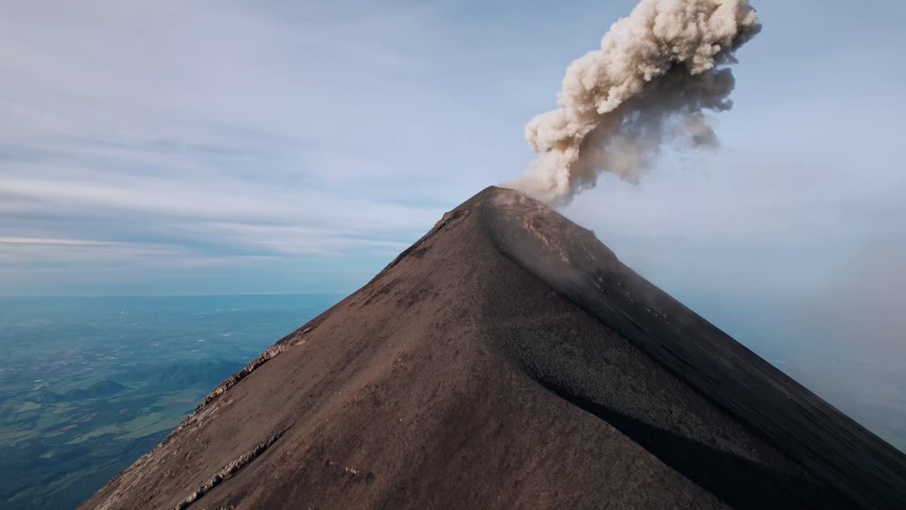 A breathtaking drone shot captures the active Volcán de Fuego in Guatemala, with a plume of ash and gas rising from its summit