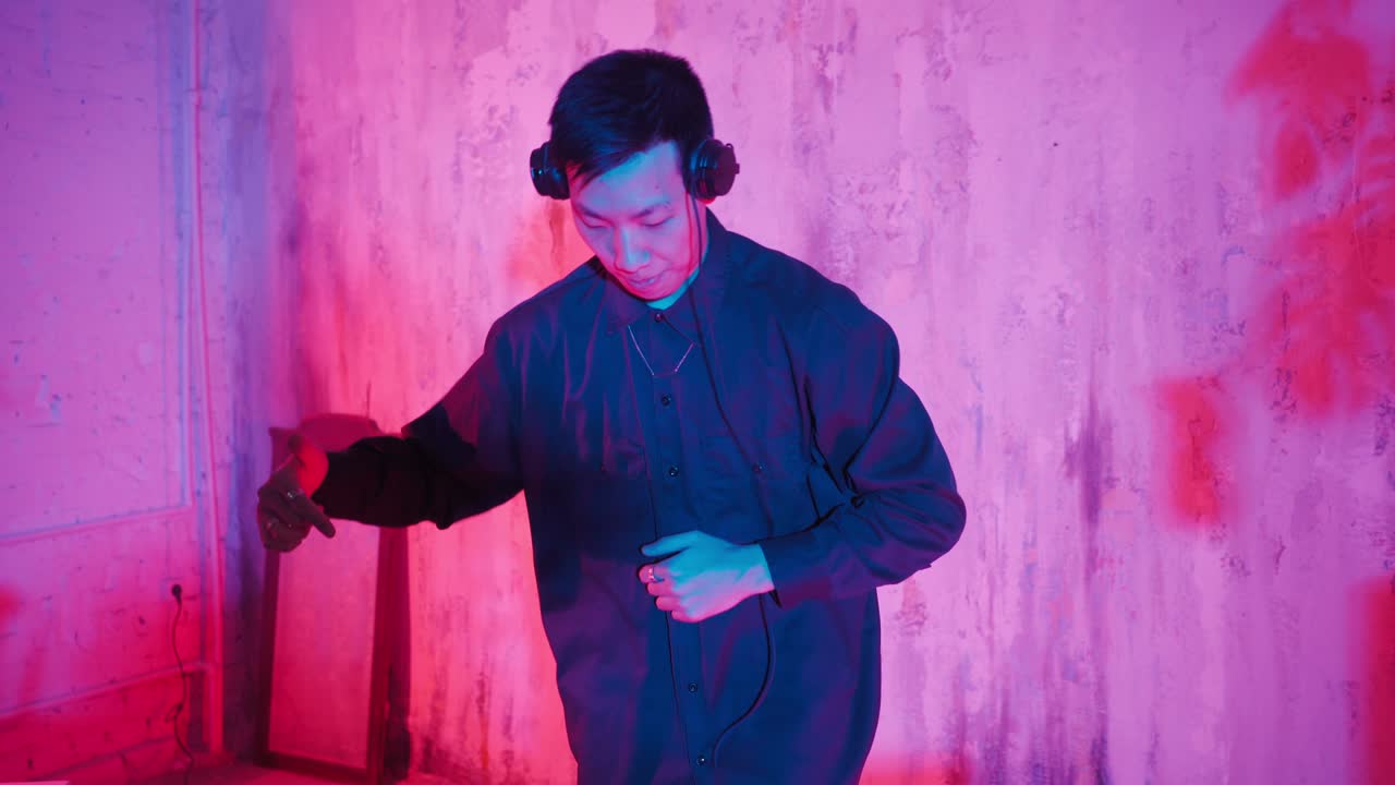 Modern DJ of Asian Appearance Performs a Music Track in Neon Lighting.