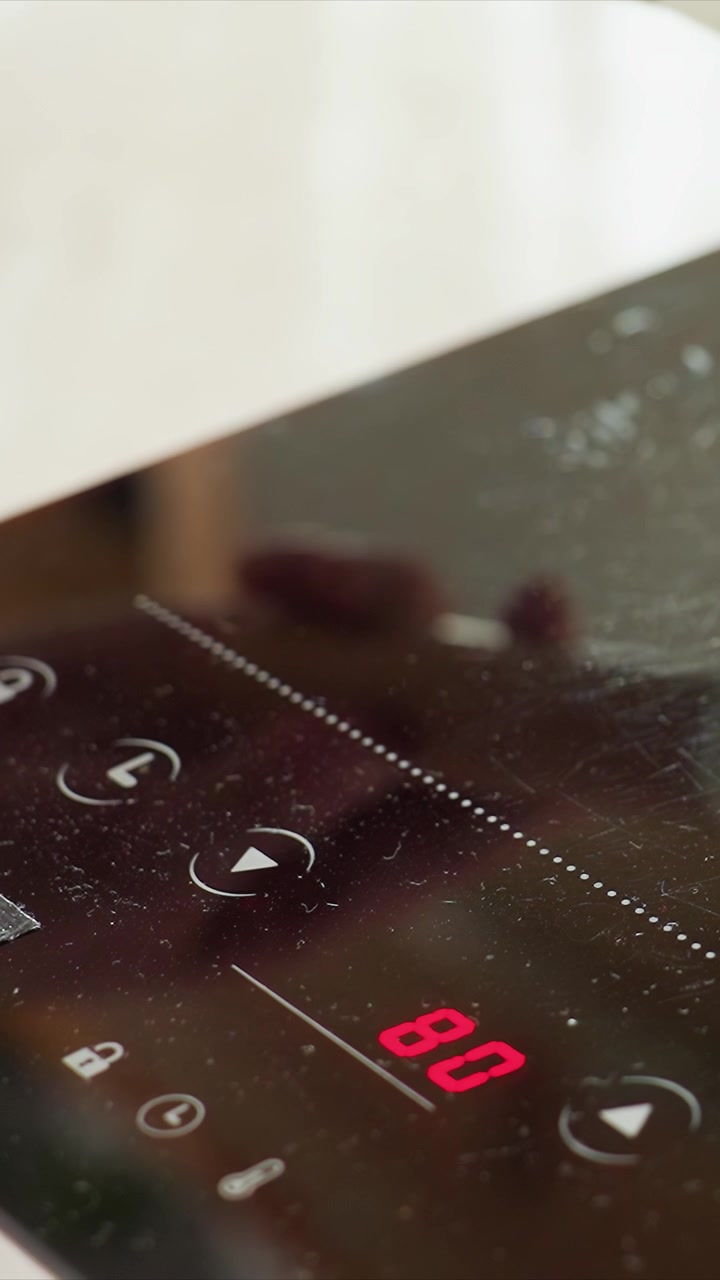 Primo piano di un pannello di controllo in vetro sensibile al tocco. Un display digitale rosso cambia tra 80 e altri valori. Piccole goccioline d'acqua suggeriscono un uso recente in un ambiente cucina